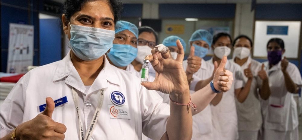 Health workers wearing PPE and masks and holding vaccine vials