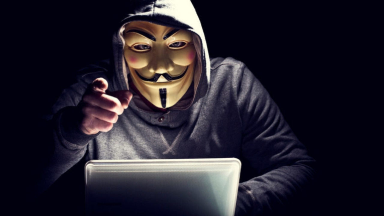 A person wearing a Guy Fawkes mask in front of his laptop