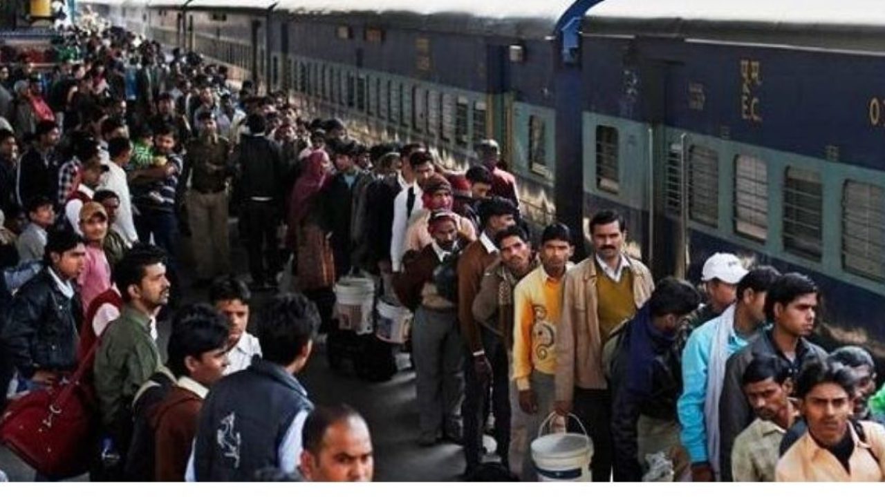 Railway passengers queue up beside parked train in a crowded railway station