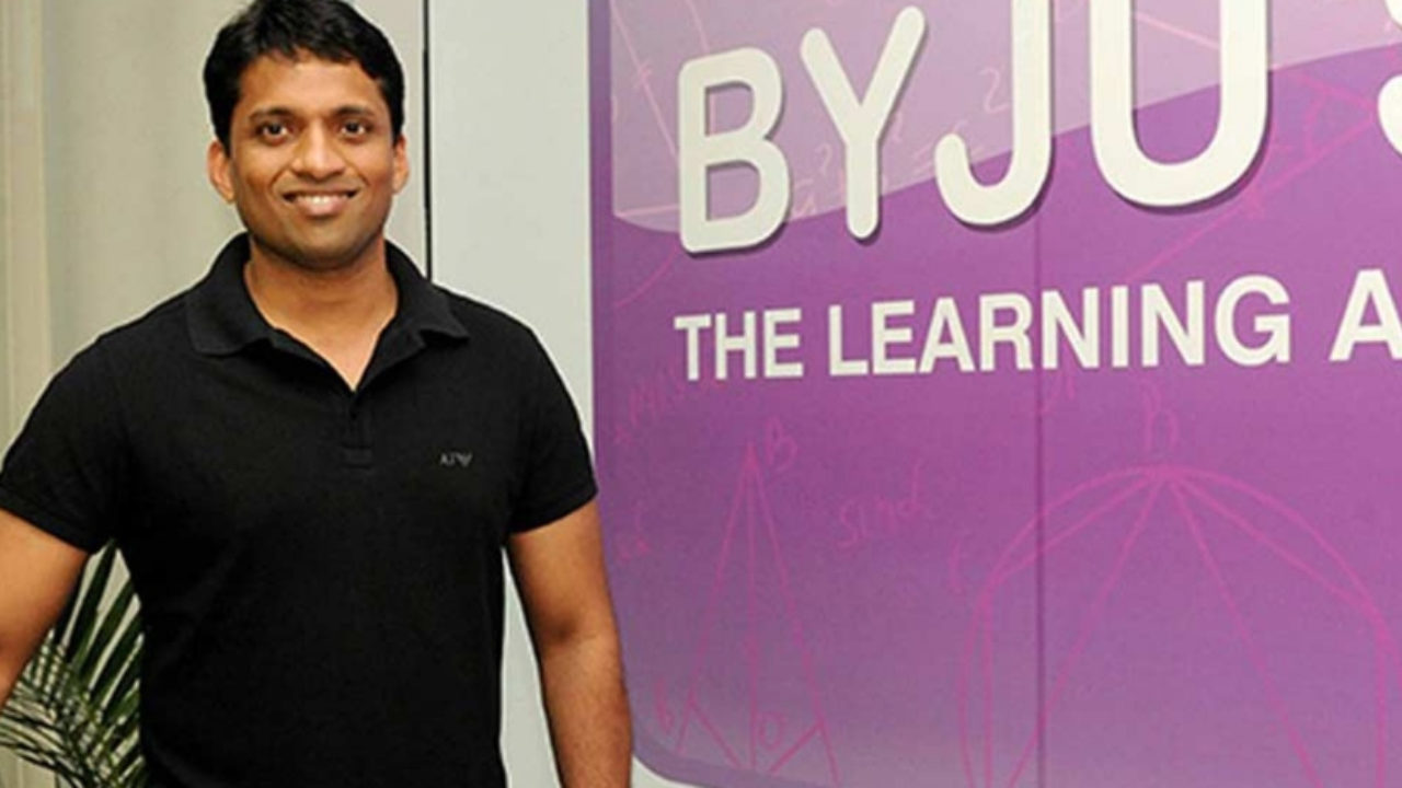 Byju's founder Byju Raveendran stands in front of BYJU'S logo on a wall
